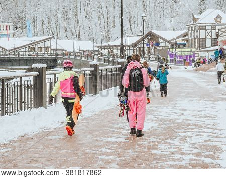 Sochi, Russia - 25 February 2020. People In Ski Suits With Equipment Walk Along The Sidewalk Along T