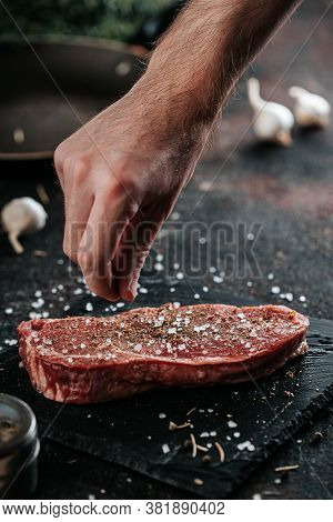 Sirloin Steak Preparation, Seasoning With Pepper And Salt. Chef Preparing Fresh Meat On Dark Marble 