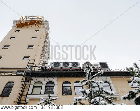 Top Of The Building With A Tower, Windows And Fire Ladders With Snow-covered Fir Trees In The Foregr