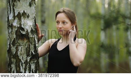 Young Caucasian Woman In The Nature. Listening The Music On The Wireless Headphones And Touching The