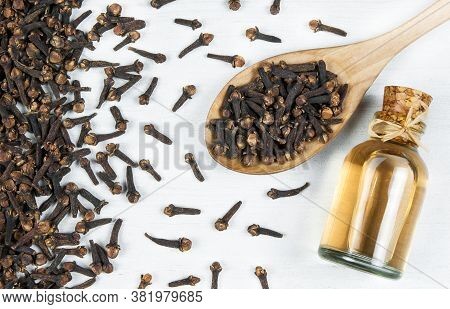 Close Up Glass Bottle Of Clove Oil And Cloves In Wooden Spoon On Wooden Table. Essential Oil Of Clov