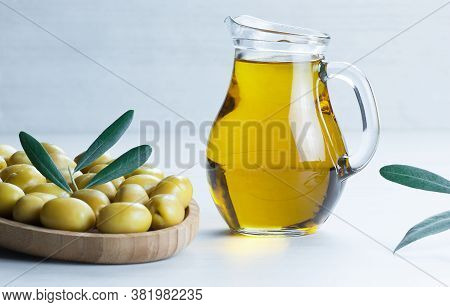 Glass Bottle Of Olive Oil And Olive Tree Branch, Raw Turkish Green Olive Seeds And Leaves On Rustic 