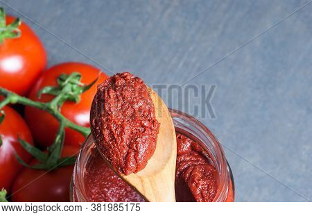 Tomato Paste In Wooden Spoon And Ripe Fresh Grape Tomatoes On Wooden Background. Cherry Tomatoes. To