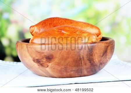 Empanadillas al horno frescos, en un recipiente de madera, en la mesa de madera, sobre fondo brillante