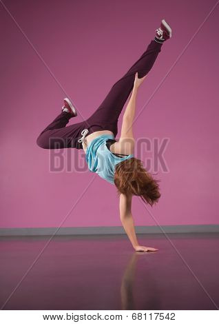 Pretty break dancer doing handstand with one hand in the dance studio