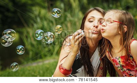 Mother And Little Girl Blowing Soap Bubbles In Park.