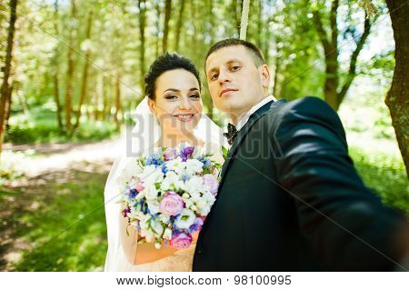 Gorgeus Wedding Couple On Green Sunny Forest. Groom Doing Selfie