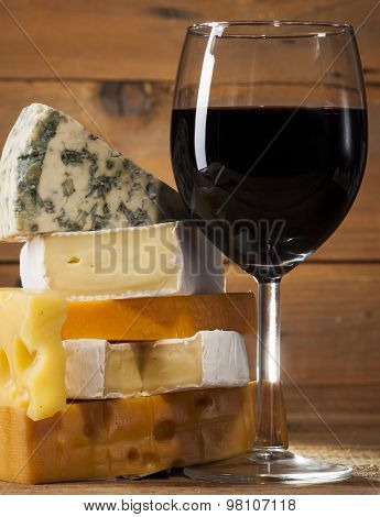 Red wine with various types of cheese on wooden background