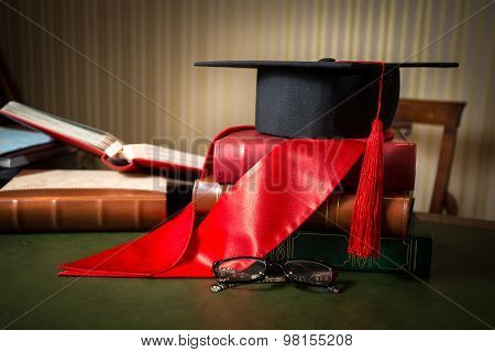 Graduation Cap And Red Ribbon Lying On Book At Library