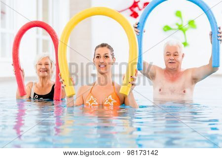 Group  or young and senior people in aquarobic fitness swimming pool exercising with  pool noodle