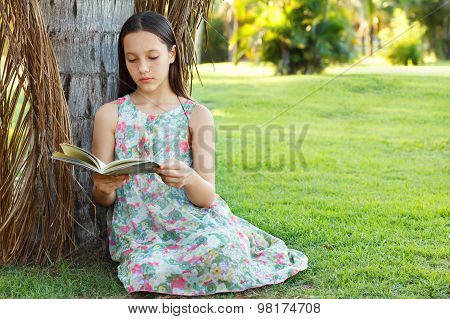 Cute Teen Girl Reading Book Sitting On Green Grass