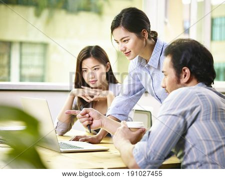 a team of young asian corporate executives discussing business in office using laptop computer.