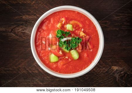 An overhead photo of gazpacho, traditional Spanish soup, garnished with jamon, tomato and onion slices, on a dark rustic background with place for text
