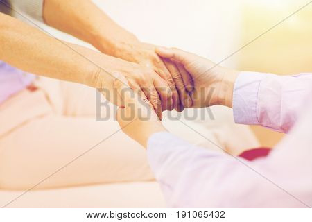 people, age, family, care and support concept - close up of senior and young woman  holding hands