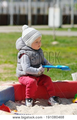 Portrait of toddler child wearing vest jacket outdoors. One year old baby boy playing with sand at playground sandbox
