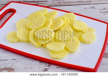 Potato cut in clices with a rib knife on a white cutting board. Step by step cooking