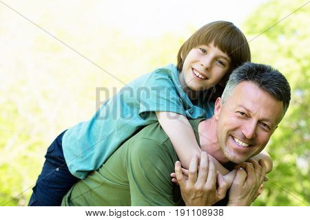 Portrait of father with his son having fun in summer park. Piggyback. Family fun. Happy boy playing with dad summer nature outdoor