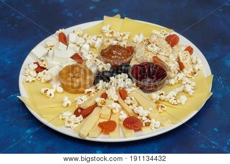 Cheese assorti with sauces and popcorn blue background