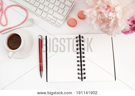Office desk table with computer, cup of coffee and peony flowers. White wooden background. Coffee break, notes or plan writing concept. Top view, flat lay.