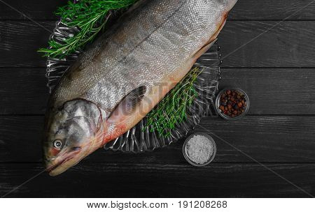 Cutting Fresh large Fish Siberian Chum salmon on glass plate dark black wooden background. Spices for fish dog-salmon pepper salt thyme tarragon knife.