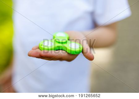 School kid playing with Tri Fidget Hand Spinner outdoors. Popular and trendy toy for hands for children and adults. Selective focus on hands of boy
