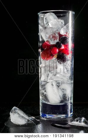 Glass of ice with berry gooseberries red black currants and water. Refreshing cocktail. Summer drink. Dark background.