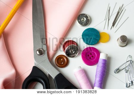 needlework and tailoring concept - scissors, sewing buttons, spools of thread, needles and cloth