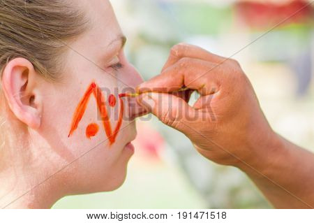 CUYABENO, ECUADOR- MAY 06, 2017: Unidentified tourist painting her face using achiote seeds from these spiny red pods with natural color, from the amazon rainforest in Cuyabeno National Park, Ecuador.