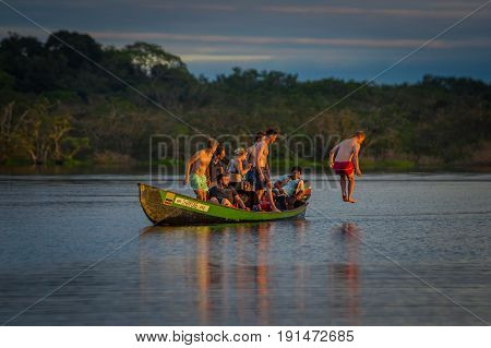 CUYABENO, ECUADOR - NOVEMBER 16, 2016: Young Tourists Jumping Into The Lagoon Grande Against The Sunset, Cuyabeno Wildlife Reserve, South America.