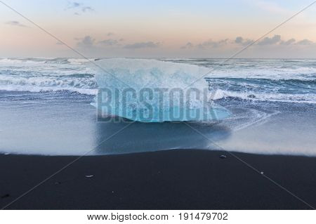 Breaking iceberg on black sand beach during late winter Iceland natural landscape background