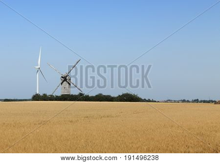 Image of a traditional windmill close to a modern eolian turbine in a cereal field.