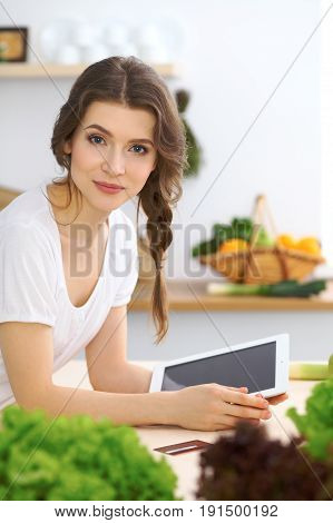 Young  woman looking for a new recipe for  cooking in a kitchen. Housewife is making online shopping by tablet computer and credit card.