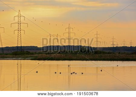 High-voltage poles reflected in the water of a lake