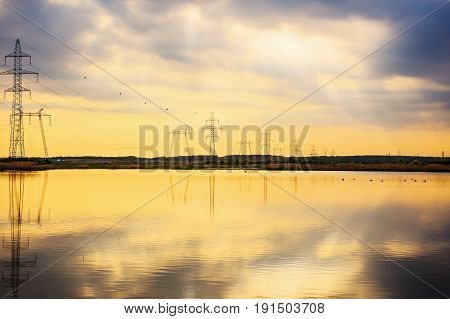 High-voltage poles reflected in the water of a lake
