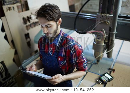 Professional engineer with touchpad standing by lathe-machine