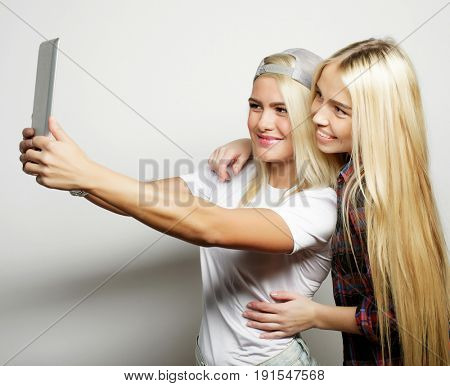 two hipster girls friends taking selfie with digital tablet, studio shot over gray vackground