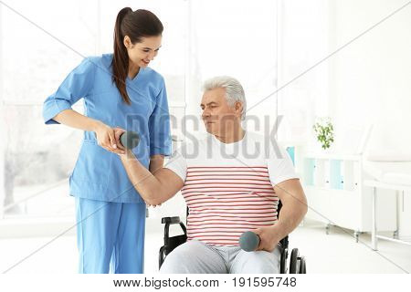 Senior disabled man with young orthopedist in rehabilitation clinic