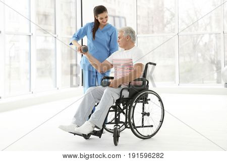 Senior disabled man with young orthopedist in rehabilitation clinic