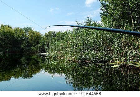 Fishing Rod On The Background Of Smooth Water Surface At Noon.