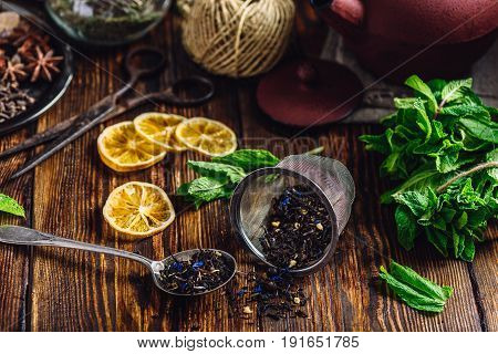 Dry Tea in Strainer and Spoonful of Tea with Fresh Mint Lemon Slices. Tangle with Two Jars and Teapot on Backdrop.
