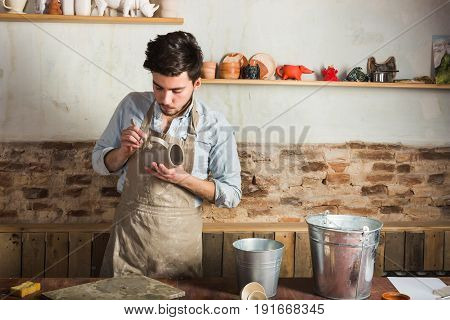 potter, workshop, ceramics art concept - young ceramist stand at a workplace with raw product, craftsman's hands holding the clay cup and tools, two buckets of water on the table, Mexican, Hispanic