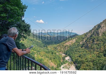 Thueyts, France, september 11, 2016: Man with newspaper in hands enjoys the view over the valley where the river Ardeche flows
