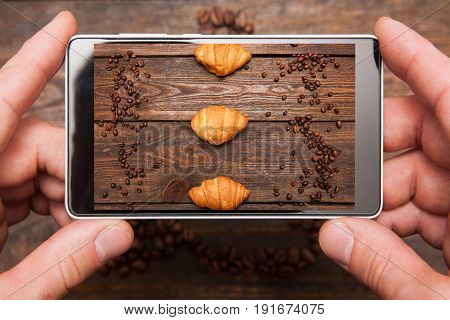 Mobile food photography. Phone in hands is shooting coffee beans and dessert on wooden background, top view