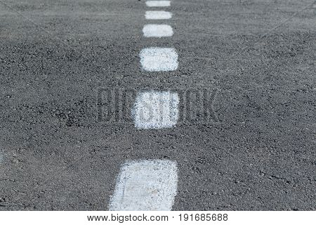 On the gray asphalt paint marking. Rough intermittent white line. Dashed markings divide the road in half.