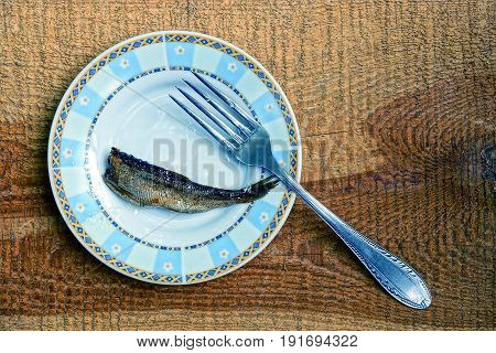 Small fish on a white plate with a fork on a wooden board