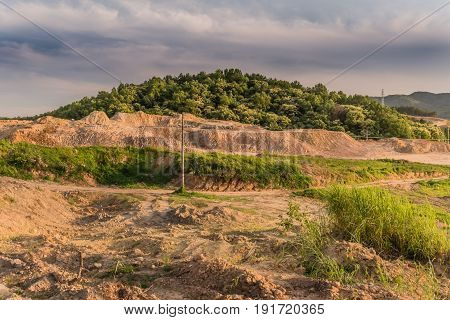Barren area of land that has been cleared for development with lush forest on a hillside.
