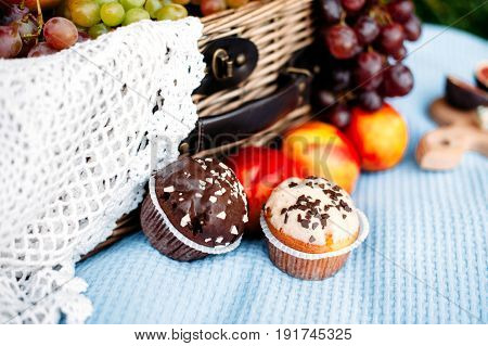 Picnic at the park delicious food. White and brown cupcakes. Picnic basket peaches grapes on the background.