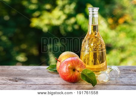 apple cider vinegar in glass decanter and ripe fresh apples on wooden table with blurred natural background