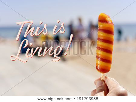 closeup of a refreshing popsicle in the hand of a young caucasian man on the beach and the text this is living