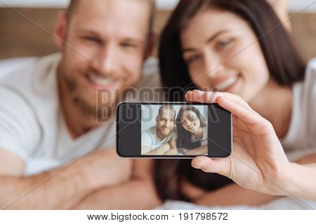 Morning selfie. Millennial man and woman grinning broadly while taking a selfie during an afternoon nap in bed.